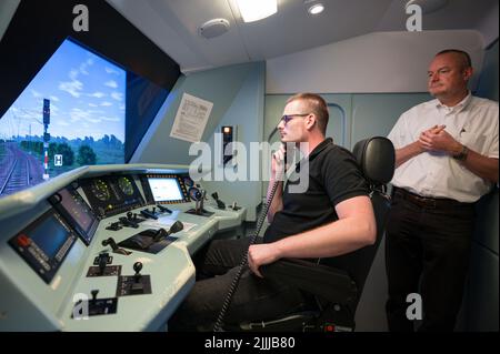 PRODUZIONE - 30 giugno 2022, Saarland, Saarbrücken: Ulrich Pietsch, capo della DB Training (r), guarda come Andreas Lutz siede al posto di guida del simulatore ferroviario a Saarbrücken. Tutti i macchinisti devono far testare ogni anno le proprie abilità di guida nel simulatore. (A dpa: 'Basta lasciare che rotoli - come i macchinisti del treno imparano a risparmiare energia') Foto: Oliver Dietze/dpa Foto Stock