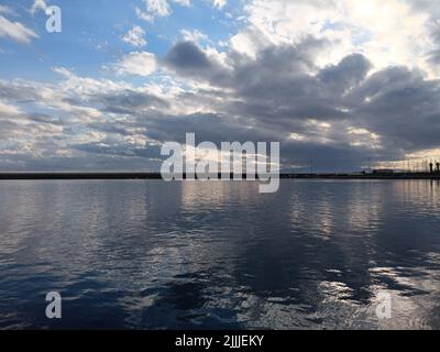 Una vista panoramica dei raggi del sole tra le nuvole nel cielo blu sopra il mare e il porto di Kalamata, Grecia Foto Stock