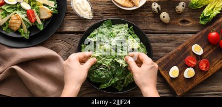 Donna che prepara gustosa Caesar insalata su sfondo di legno, vista dall'alto Foto Stock