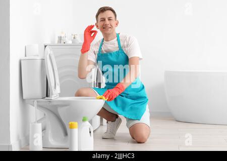 Il ragazzo pulisce la tazza del gabinetto e mostra OK in bagno Foto Stock