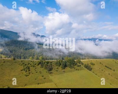 Summer day in the Ukrainian Carpathians. The old mountains are covered with forest. Low clouds hang over the valley. Hayfields on the slope of the mou Foto Stock