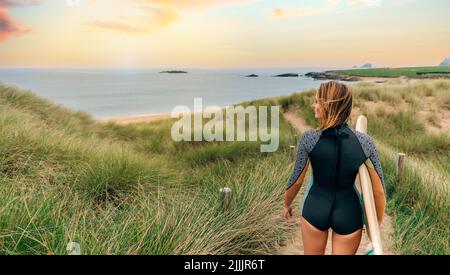 Donna surfista con muta e surf andando alla spiaggia attraverso le dune Foto Stock