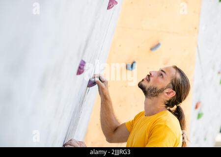 Un uomo sportivo in una t-shirt gialla sale su un muro di arrampicata. Foto Stock