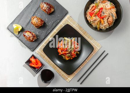 Una varietà di piatti asiatici su sfondo giallo chiaro. Verdure fritte cinesi con altri piatti asiatici su sfondo grigio. Pollo teriyaki e. Foto Stock