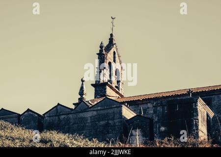 Particolare della Chiesa e cimitero di un villaggio galiziano sotto il tramonto da una collina. Foto Stock