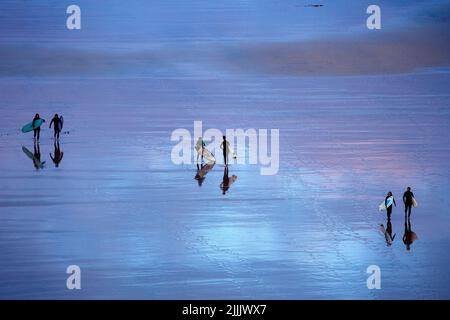 I surfisti britannici tornano a casa attraverso una splendida spiaggia turchese dopo una lunga giornata di surf sulle onde a Carbis Bay in Cornovaglia nel Regno Unito Foto Stock