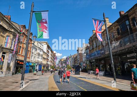 Persone a piedi pedonale St Mary Street, bandiere battenti per il giubileo della Regina in una giornata di sole. A Cardiff, Galles, Regno Unito. Foto Stock