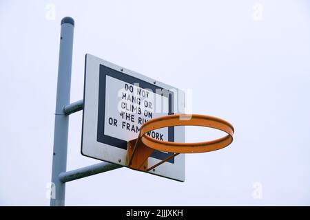 Un cerchio di basket senza rete, in un parco pubblico. Il backboard ha un avvertimento circa appeso sul bordo, telaio, non danneggiare, romperlo. A Cardiff Foto Stock