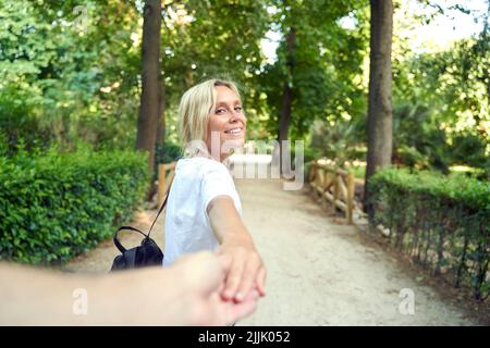 Donna bionda che cammina nel parco, tira la mano del suo ragazzo. Concetto di coppia Foto Stock