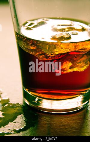 Bicchiere di whiskey con ghiaccio, su un tavolo bagnato. Foto Stock