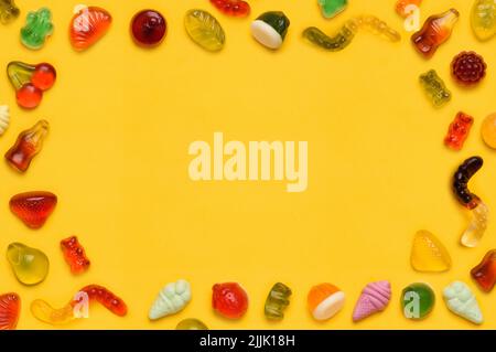 Cornice gommosa bordo, gelatina assortita gomma frutta caramelle caramelle caramelle su sfondo giallo vista dall'alto piatto Foto Stock