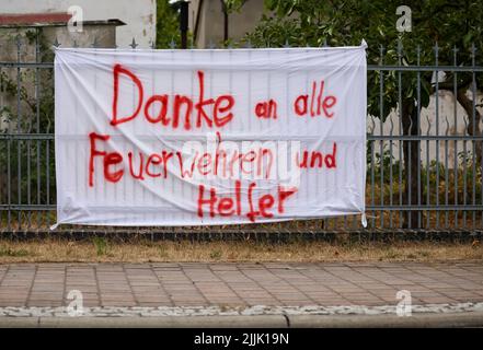 Falkenberg, Germania. 27th luglio 2022. Un banner che legge 'grazie a tutti i vigili del fuoco e aiutanti' appende su una recinzione. I vigili del fuoco di Brandeburgo continuano a combattere un grande incendio boschivo nel distretto di Elbe-Elster. Da lunedì (25,07.) brucia su una superficie di 800 ettari. Le aree sono parzialmente contaminate da munizioni. Questo complica il lavoro di estinzione degli incendi. Credit: Jan Woitas/dpa/Alamy Live News Foto Stock