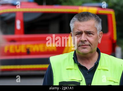 Falkenberg, Germania. 27th luglio 2022. Steffen Ludewig, capo del distretto dei vigili del fuoco, si trova di fronte a un camion dei vigili del fuoco. I vigili del fuoco di Brandeburgo continuano a combattere un importante incendio boschivo nel distretto di Elbe-Elster. Da lunedì (25,07.) brucia su una superficie di 800 ettari. Le aree sono parzialmente contaminate da munizioni. Questo complica il lavoro di estinzione degli incendi. Credit: Jan Woitas/dpa/Alamy Live News Foto Stock