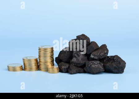 Carbone nero duro con pile di monete su sfondo blu, concetto di prezzo dei combustibili fossili Foto Stock