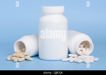 Flaconi bianchi per medicinali, uno chiuso e due con pillole versate su sfondo blu con spazio copia Foto Stock