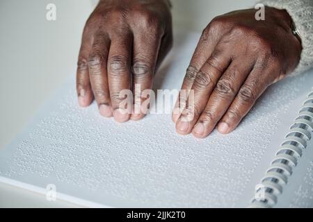 Alto angolo di visione dell'anziano africano che usa le sue mani per leggere il braille al tavolo Foto Stock