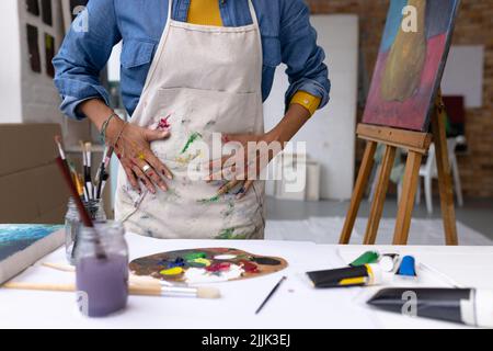 Immagine della sezione centrale dell'artista biraciale femminile in grembiule con pennelli in studio Foto Stock