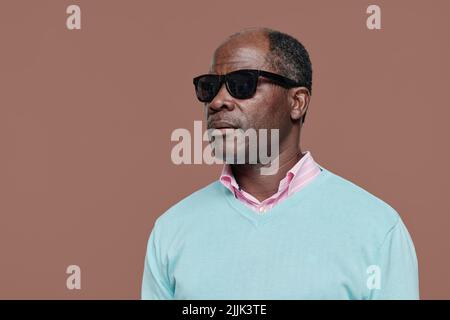 Ritratto di un uomo cieco maggiore africano in vetri scuri su sfondo marrone Foto Stock