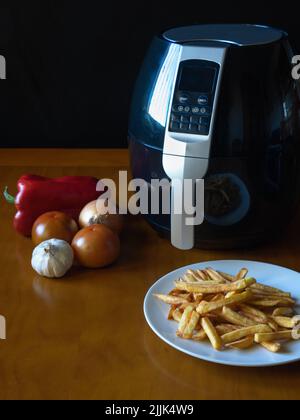 Friggitrice ad aria su un tavolo con patatine fritte e verdure. Concetto di cibo sano Foto Stock