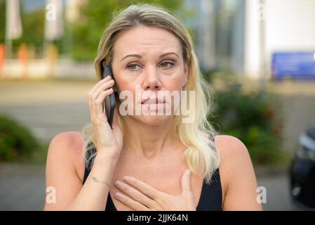 Donna che guarda stressata mentre ascolta una chiamata sul suo cellulare all'aperto su una strada cittadina Foto Stock