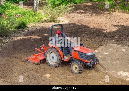 Un agricoltore su un mini trattore allenta il terreno per il prato. Coltivazione di terra, livellamento di superficie. Foto Stock