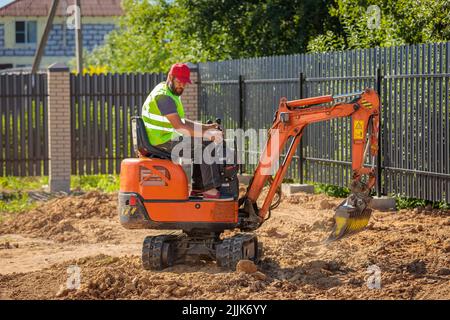 Un uomo su un miniescavatore livella un pezzo di terra, allenta il terreno Foto Stock