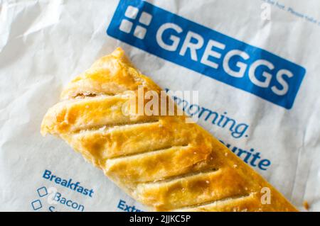 Il rotolo di salsiccia di Greggs è posto sopra un sacchetto di carta stampato di Greggs Foto Stock