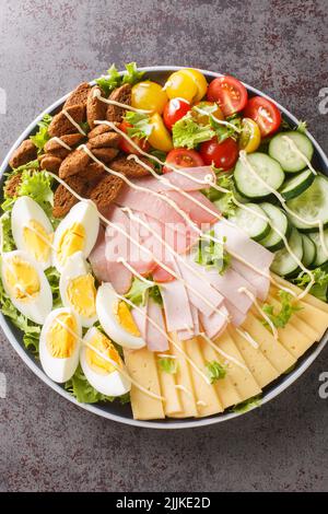 Bella e deliziosa Chef Salad con uova. Prosciutto, formaggio, pomodori freschi, cetrioli e crostini stagionati primo piano nel piatto sul tavolo. Vertica Foto Stock