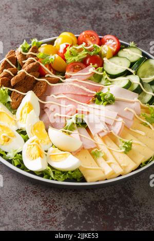 Bella e deliziosa Chef Salad con uova. Prosciutto, formaggio, pomodori freschi, cetrioli e crostini stagionati primo piano nel piatto sul tavolo. Vertica Foto Stock