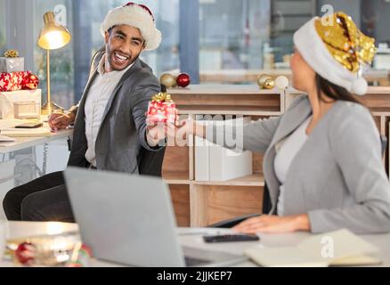 Forse stiamo lavorando, ma abbiamo ancora un tempo brutto: Un giovane uomo d'affari e una donna d'affari che scambiano regali di Natale in un ufficio moderno. Foto Stock