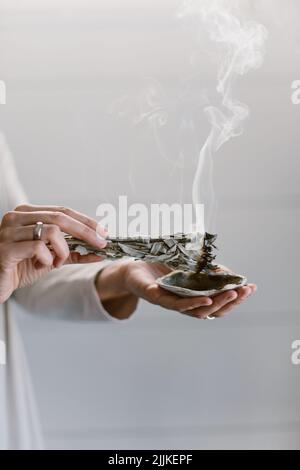 Un colpo verticale di una donna che brucia salvia e la tiene sopra una conchiglia. Foto Stock