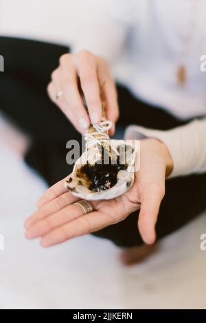 Un primo piano verticale di una donna che brucia salvia e la tiene sopra una conchiglia. Foto Stock