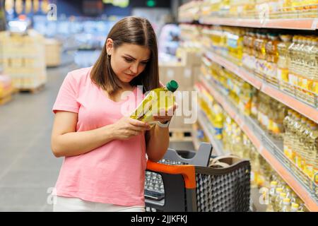 Giovane ragazza graziosa sta facendo shopping in un grande deposito. La ragazza acquista generi alimentari al supermercato. Bella ragazza sorridente in abiti casual sta tenendo t Foto Stock