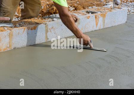 Un operaio di muratura tiene una cazzuola d'acciaio mentre leviga calcestruzzo intonacato su un pavimento di cemento Foto Stock
