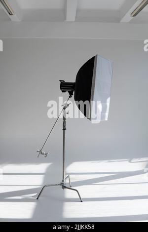 Flash fotografico professionale con un grande softbox su uno stand a C su un ciclorama in un moderno studio fotografico con grandi finestre. Illuminazione professionale Foto Stock