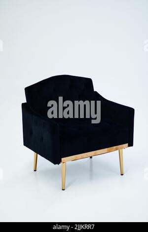 Un colpo verticale di una poltrona in velluto nero con gambe dorate su sfondo bianco Foto Stock