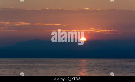 Il sole si trova dietro la grande montagna del Lago di Garda Foto Stock