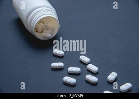 Primo piano di un flacon con pillole bianche isolate su sfondo scuro. Foto Stock
