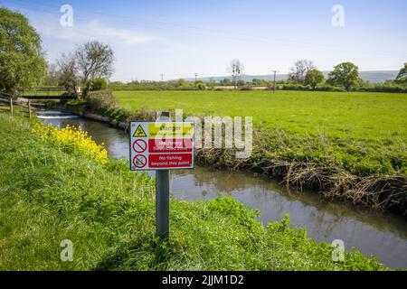 Un segnale di avvertimento sui pericoli dei cavi elettrici in testa sulla riva del fiume Yeo, anche noto come il Congresbury Yeo, a Iwood vicino Congresbury, North Somerset, Inghilterra. Foto Stock
