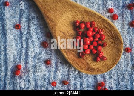 Una vista dall'alto di palle di pepe rosso su un cucchiaio di legno e una superficie di un panno blu Foto Stock