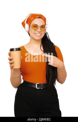 Una foto di una giovane donna che tiene una tazza di caffè e ascolta la musica mentre guarda e sorride la fotocamera Foto Stock