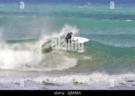 Un surfista che esegue una svolta superiore su un'onda a Fistral Beach Foto Stock