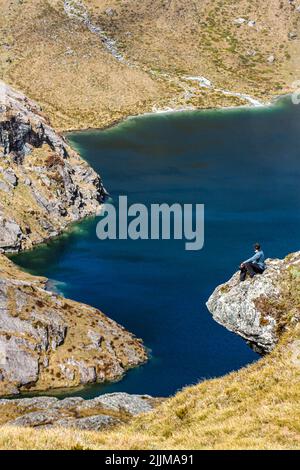 Un colpo verticale di un giovane maschio seduto su una scogliera su una costa del lago in una giornata di sole Foto Stock