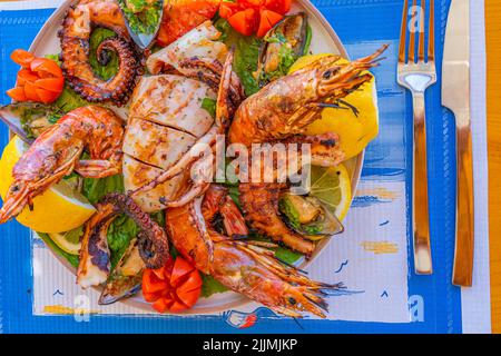 Piatto di pesce con calamari alla griglia, polpo, gamberi e cozze su insalata verde con limone e pomodoro Foto Stock