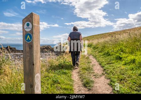 Una freccia di percorso e direzione con una donna che cammina lungo il sentiero costiero Fife a St Monans nel Neuk orientale di Fife, Scozia. Foto Stock