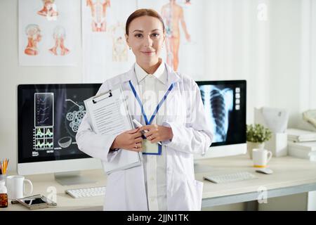 Ritratto di medico sorridente in piedi in ufficio medico con documento in mano Foto Stock