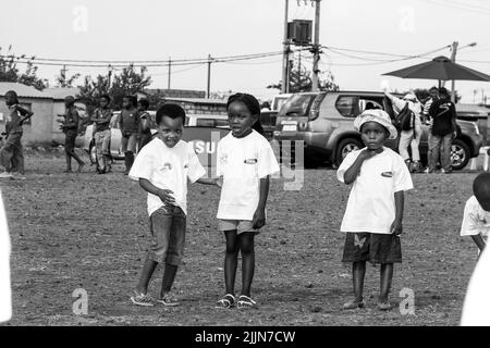 Una scala di grigi di bambini africani che svolgono attività legate al calcio nel campo scolastico di Johannesburg, Sudafrica Foto Stock