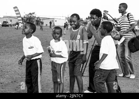 Una scala di grigi di bambini africani che svolgono attività legate al calcio nel campo scolastico di Johannesburg, Sudafrica Foto Stock
