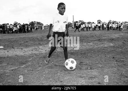 Una scala di grigi di un bambino africano che fa le attività relative al calcio sul campo di gioco della scuola a Johannesburg, Sudafrica Foto Stock