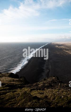 Una vista panoramica della spiaggia di kirkjufjara contro il cielo nuvoloso blu nella luce del sole nel sud dell'Islanda Foto Stock